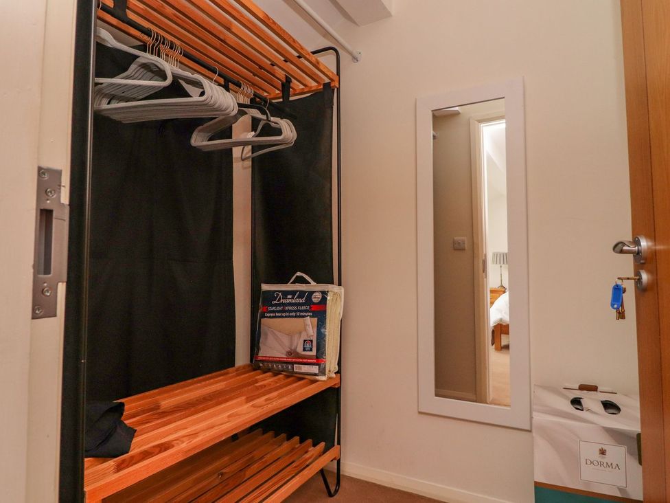 A small closet with wooden shelves hangers and a mirror on the wall at High View Meadows in Kirkby Lonsdale