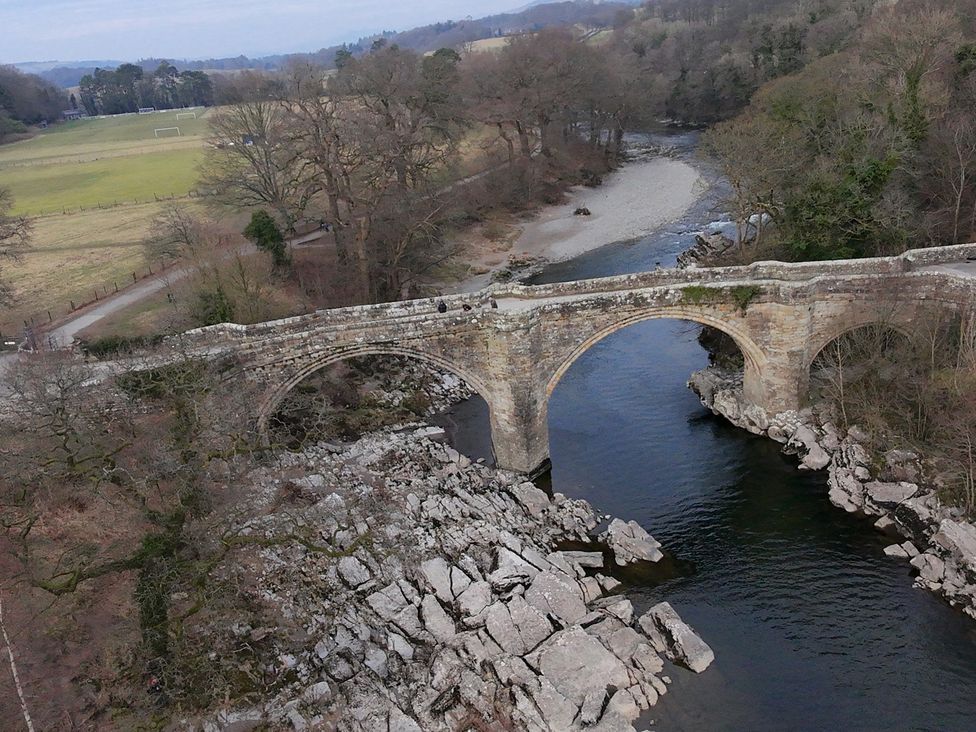 A bridge over a river with surrounding rocks and trees at High View Meadows in Kirkby Lonsdale