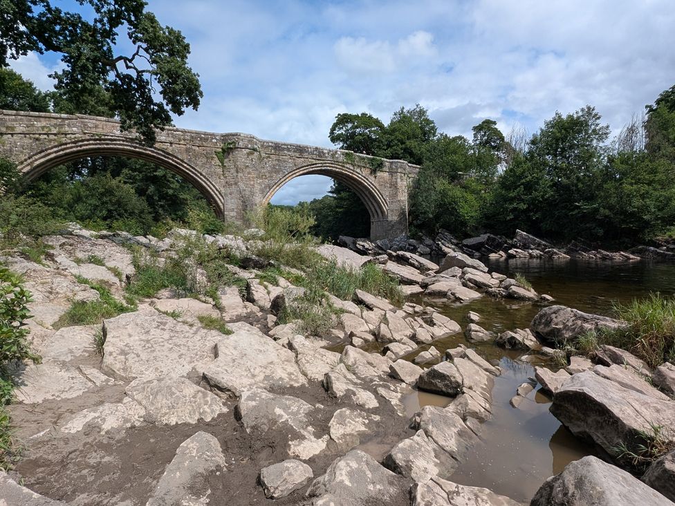 A bridge over a river with rocks and vegetation at High View Meadows in Kirkby Lonsdale
