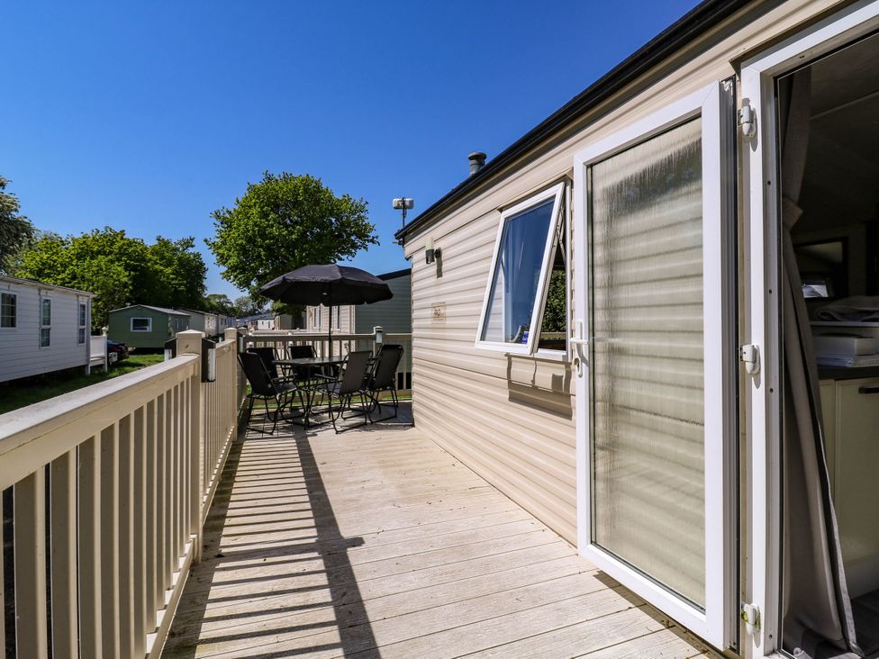 An outdoor deck area with a table and chairs under an umbrella attached to a beige caravan at Caravan 941 in Clacton-On-Sea