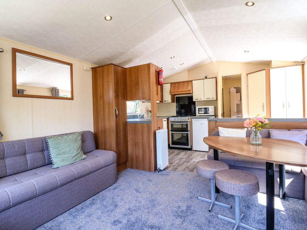 A living area with a sofa, table with stools, kitchen appliances, and wooden cabinets at Caravan 941 in Clacton-On-Sea