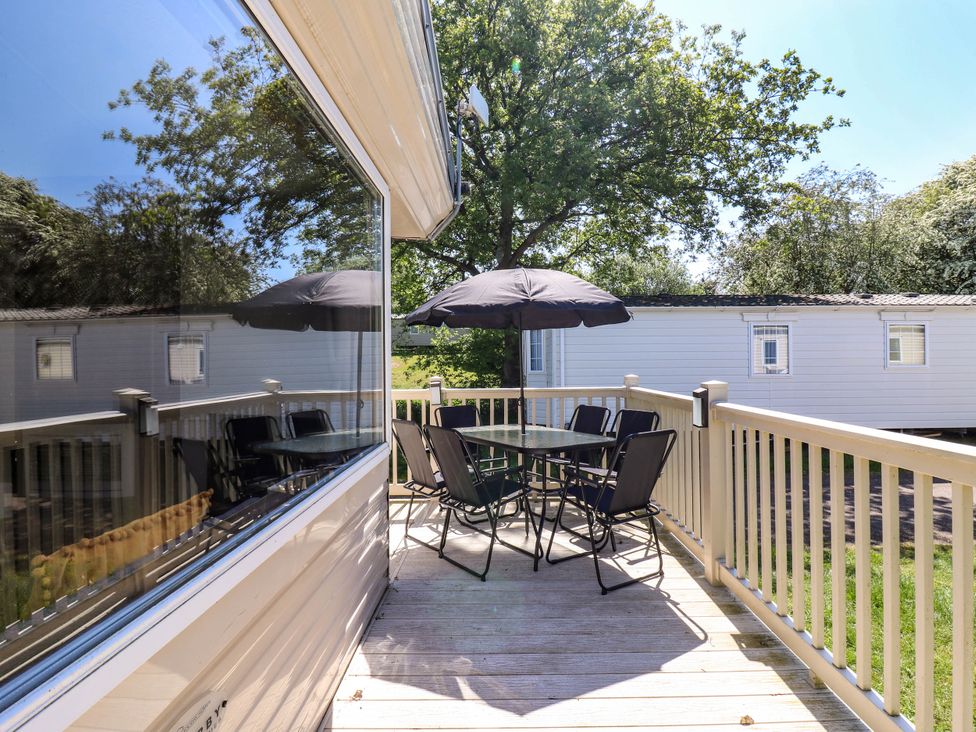 An outdoor deck with a table six chairs and an umbrella next to a white caravan at Caravan 941 in Clacton-On-Sea