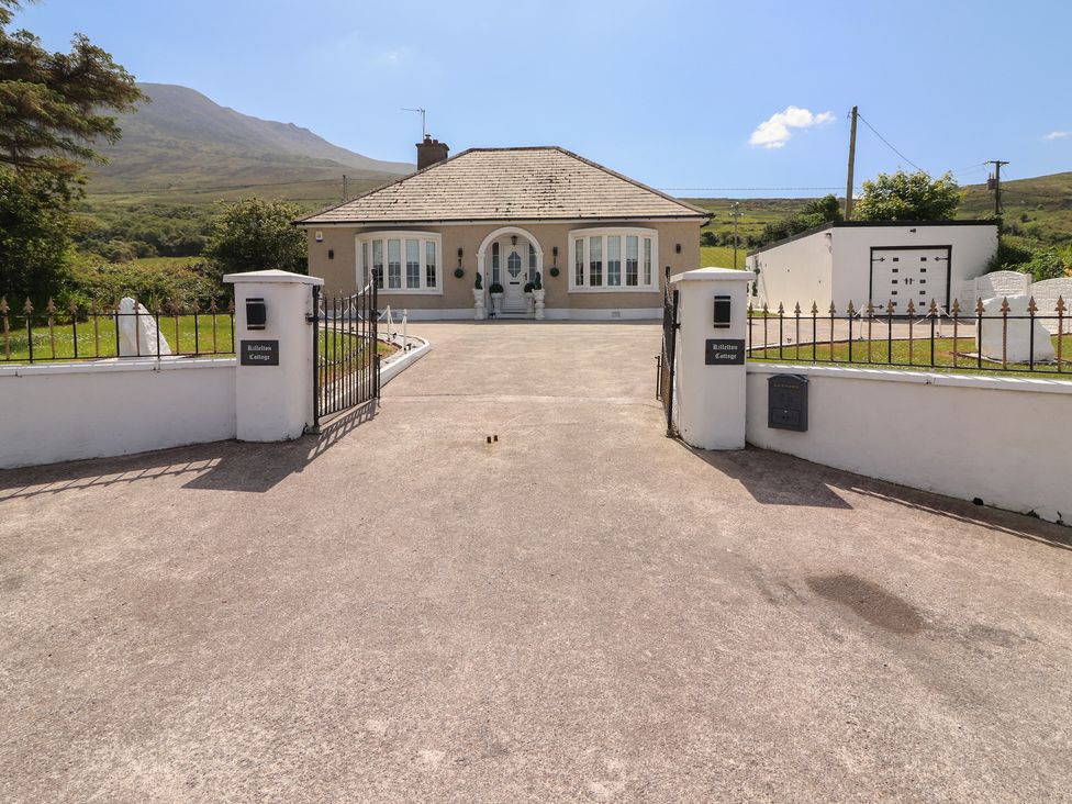 A bungalow house with a driveway and gated entrance set against a mountain backdrop at Killelton Cottage in Camp County Kerry