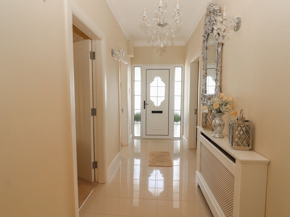 A hallway with a white front door two open doorways a chandelier a decorative mirror a radiator cover with flowers and lanterns on top