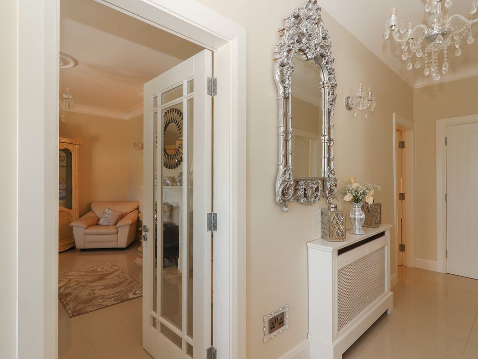 A hallway with a decorative silver-framed mirror above a white radiator cover and a view into a living room with a beige armchair and a cabinet at Killelton Cottage in Camp County Kerry