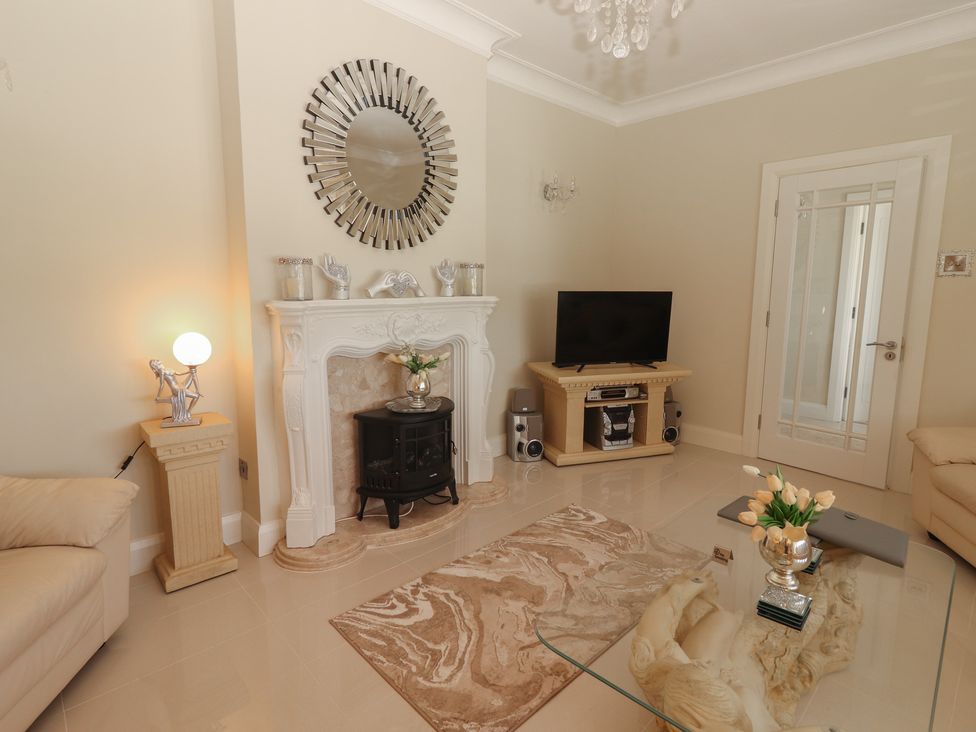 A living room with a glass coffee table with flowers on it a decorative fireplace a television on a stand and beige sofas at Killelton Cottage in Camp County Kerry
