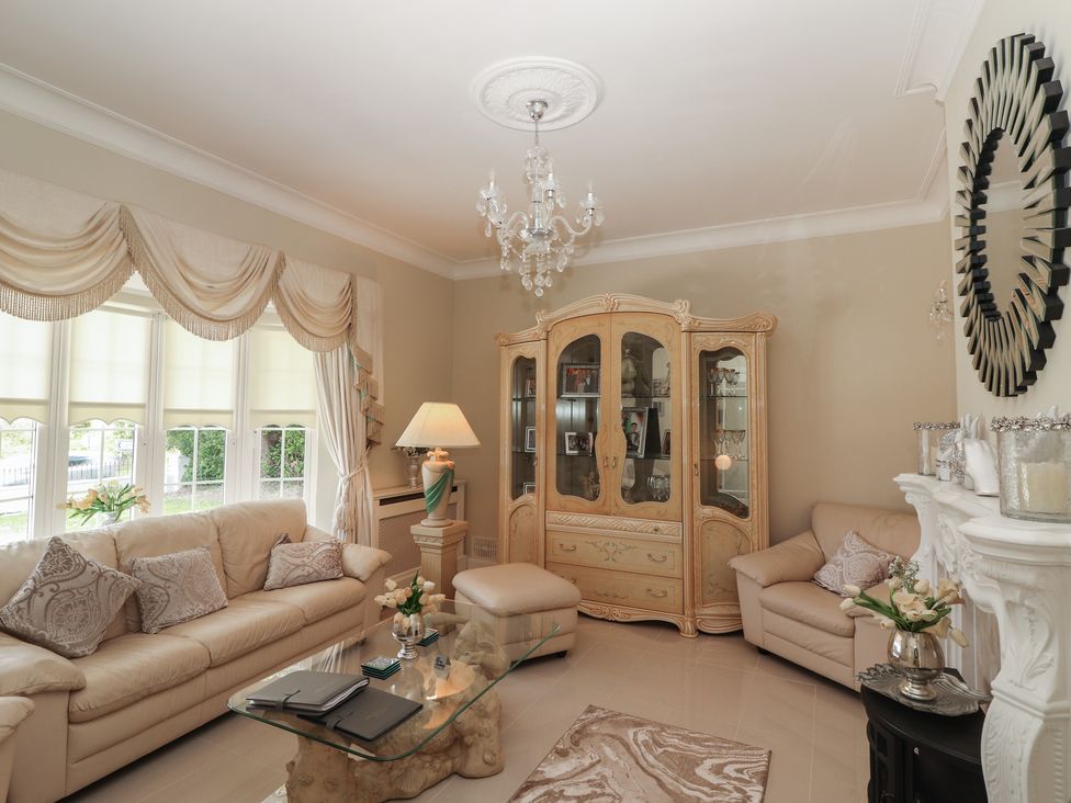 A living room with beige sofas a glass coffee table a decorative cabinet and a chandelier at Killelton Cottage Camp County Kerry