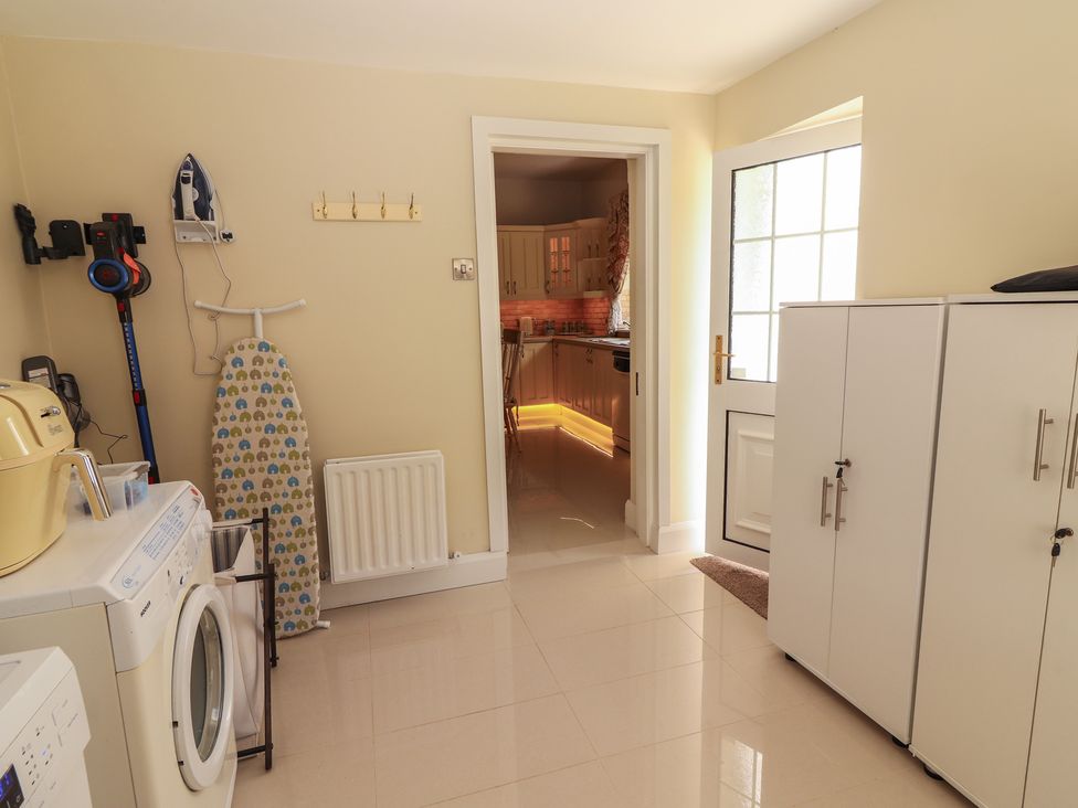 A utility room with a washing machine ironing board cabinets and a doorway leading to a kitchen at Killelton Cottage in Camp County Kerry