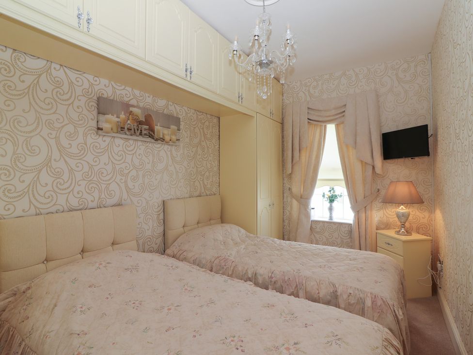 A bedroom with two single beds a chandelier built in cupboards curtains bedside table with lamp and a wall mounted television at Killelton Cottage in Camp County Kerry
