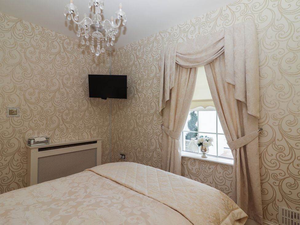 A bedroom with patterned wallpaper a mounted television ornate curtains and a bed at Killelton Cottage Camp County Kerry