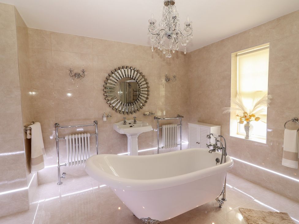 A bathroom with a freestanding bathtub a pedestal sink a round mirror and a window with flowers at Killelton Cottage Camp County Kerry