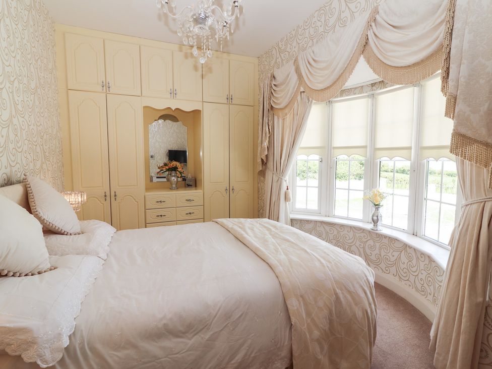 A bedroom with a bed next to a bay window with curtains and built-in wardrobes with a mirror at Killelton Cottage in Camp County Kerry