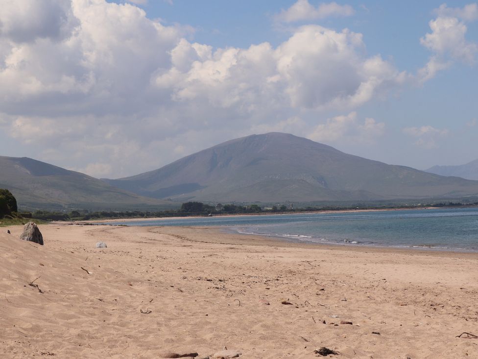 A sandy beach with water and mountains in the background under a partly cloudy sky