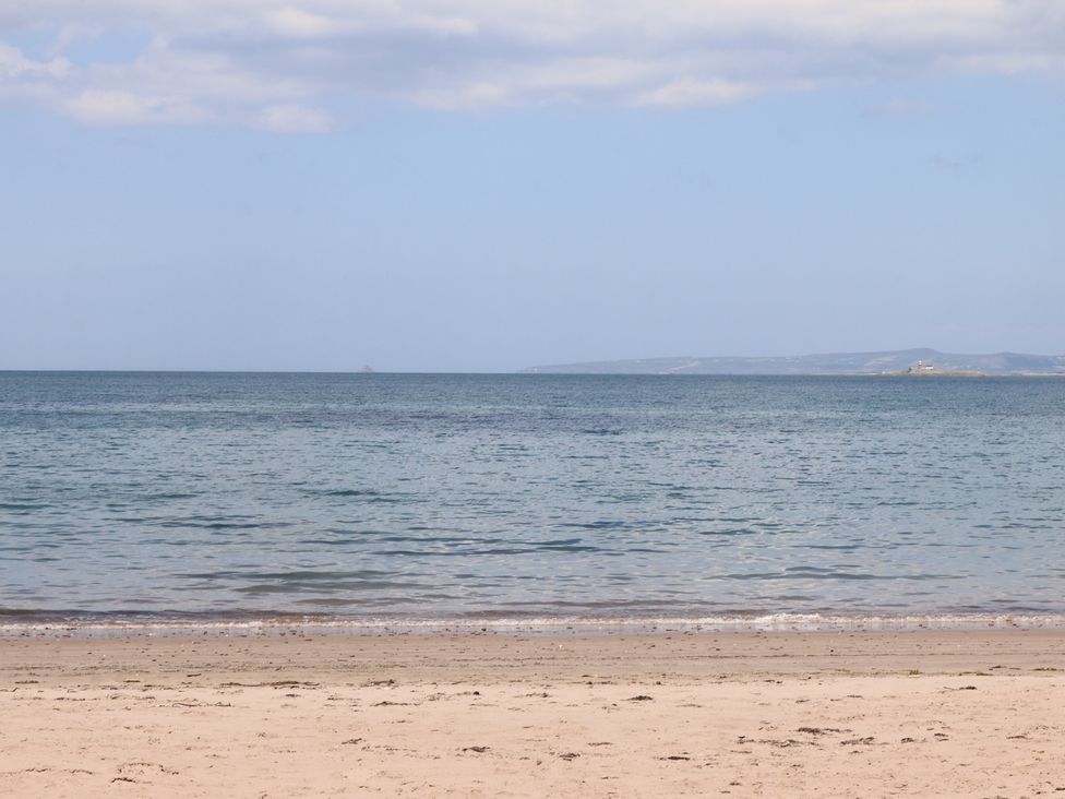 A sandy beach with calm sea water and a distant coastline under a partly cloudy sky at Killelton Cottage in Camp County Kerry