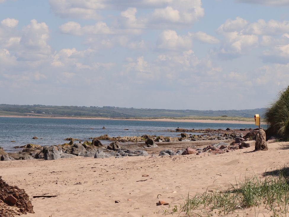 A sandy beach with rocks along the shore and water with a distant green landscape under a partly cloudy sky at Killelton Cottage in Camp County Kerry