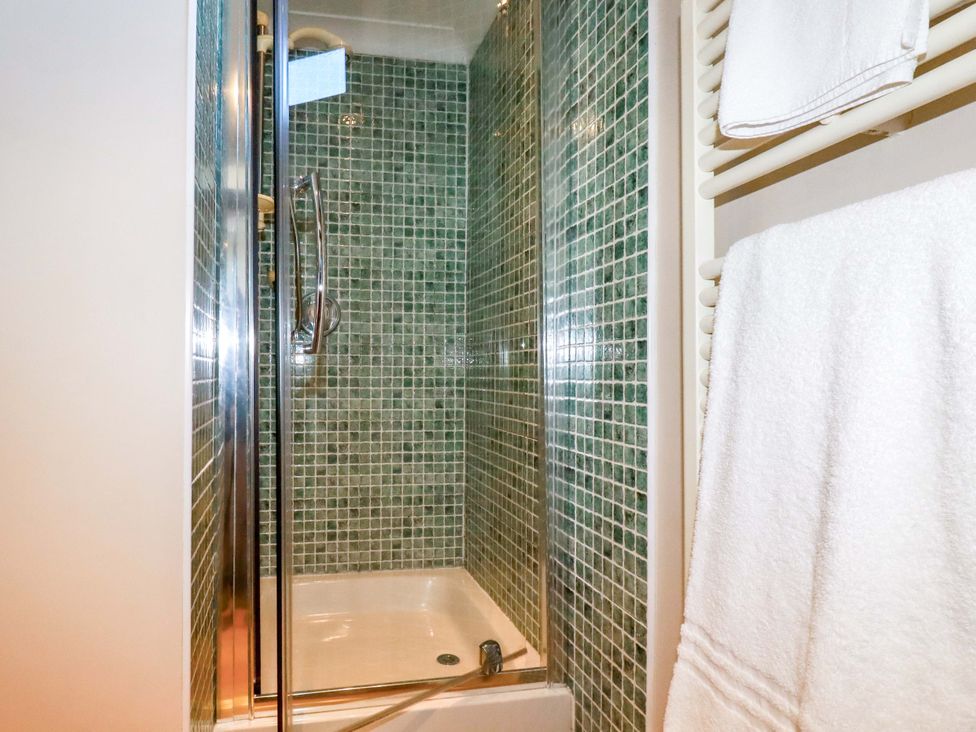 A shower enclosure with tiled walls and towels at The Coach House in Falmouth