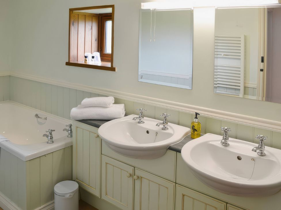 A bathroom with two wash basins and a bath tub at The Coach House Budock Water near Falmouth