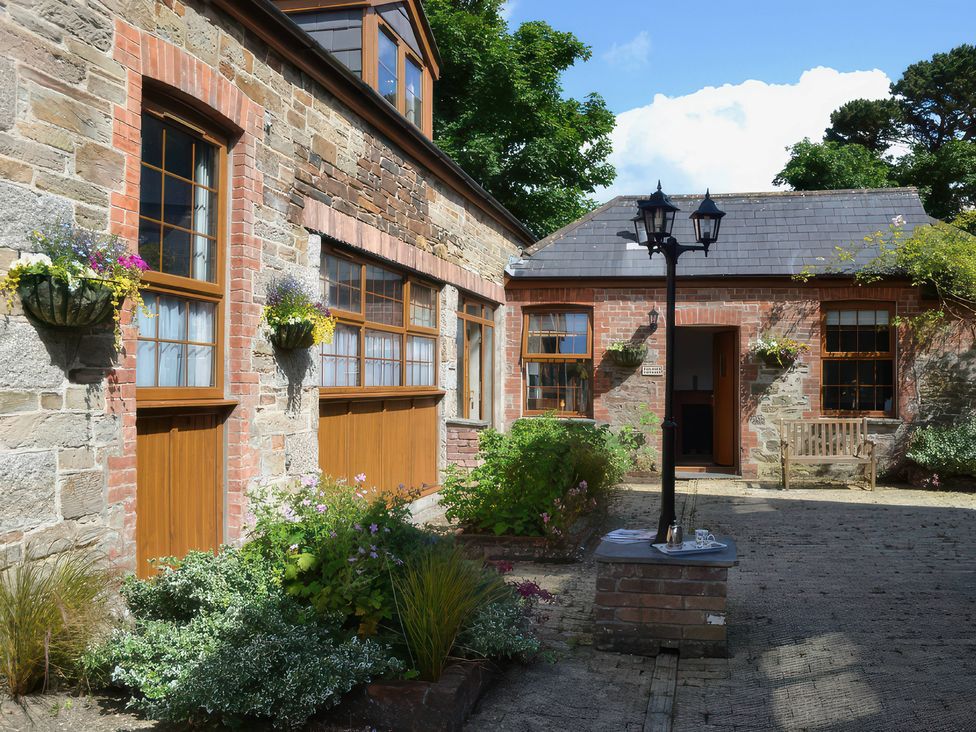 An outdoor area with brick walls, wooden doors, and flower pots at The Coach House Budock Water near Falmouth