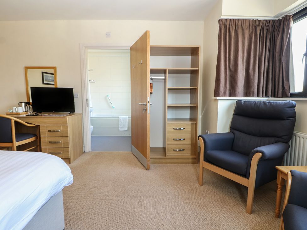 A bedroom with a bed, chair, table, television and wardrobe at Bedroom 10 in Littlehampton