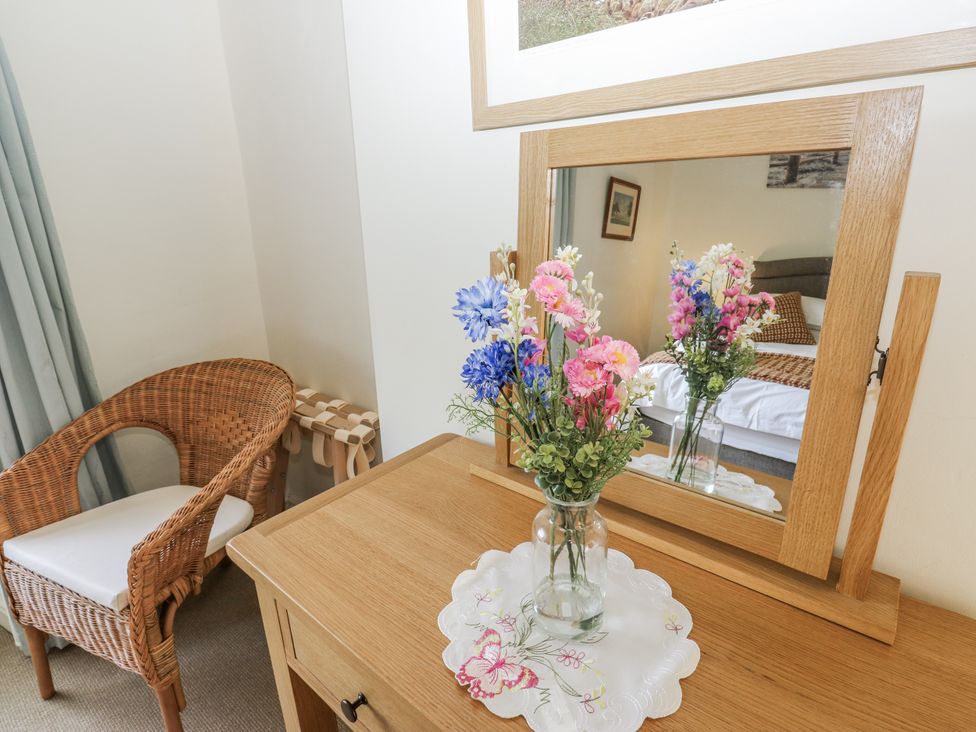 A table with flowers and a mirror in a bedroom at Centenary Cottage in Skipton