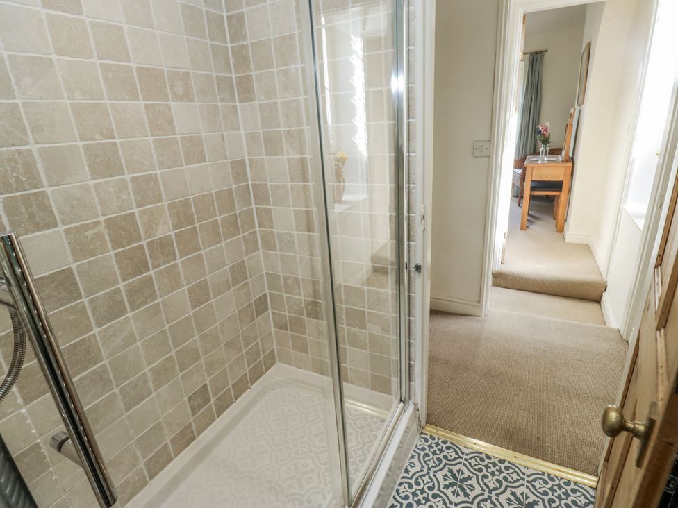 A bathroom with a shower and a view to the hallway at Centenary Cottage in Skipton