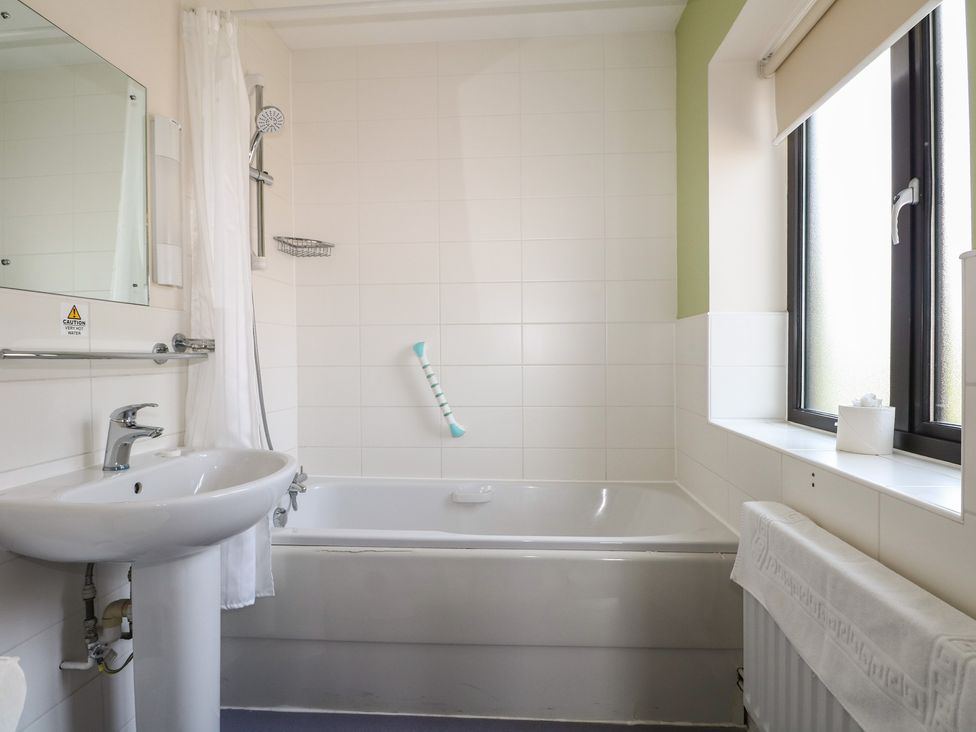 A bathroom featuring a bathtub, sink, mirror, and window at Bedroom 18 in Littlehampton
