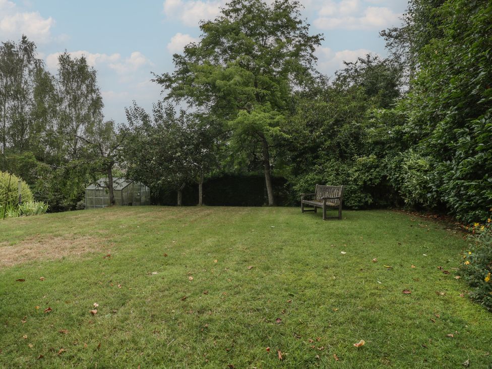 A garden with grass, trees, a bench and a greenhouse at St. Marys House Church Westcote near Bledington