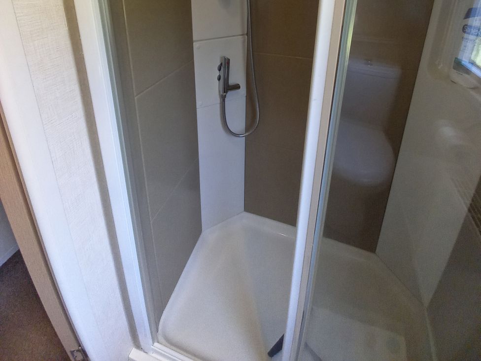 A shower with a showerhead and tiled wall at Emma No.6 in Llandegfan