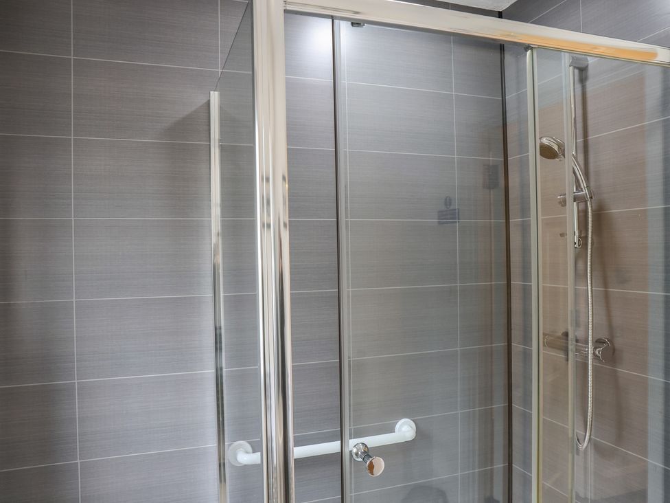 A shower with glass doors and showerhead at Bungalow 15 Eamont Park Penrith