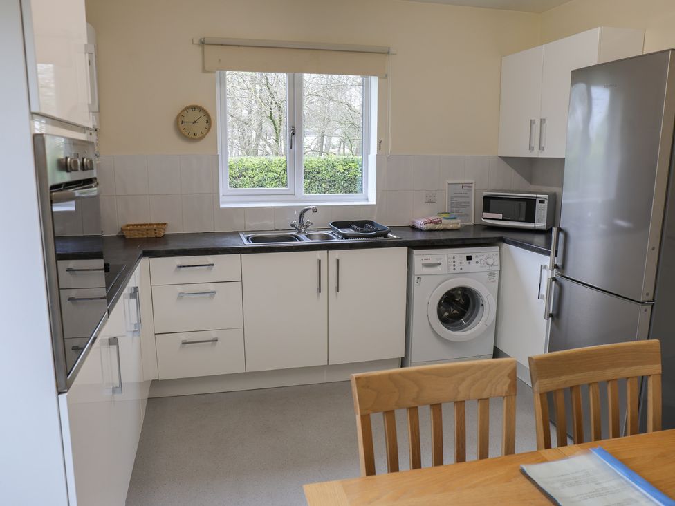 A kitchen with cabinets, sink, washing machine, microwave, and dining table at Bungalow 14 Eamont Park in Penrith