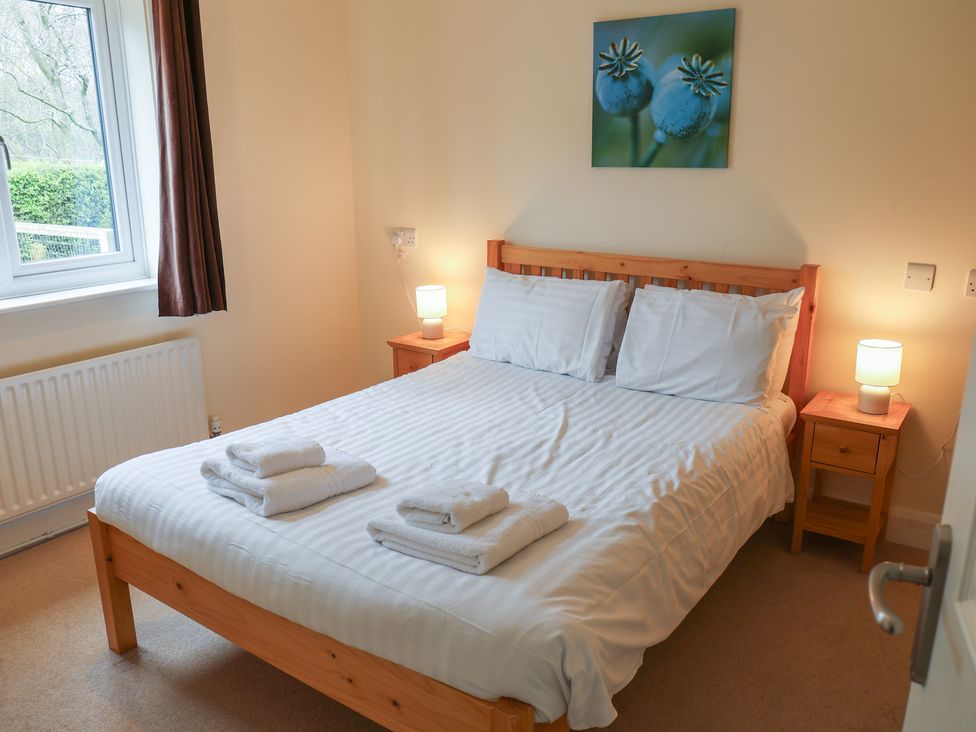 A bedroom with a bed, bedside tables, and a window at Bungalow 14 Eamont Park Penrith