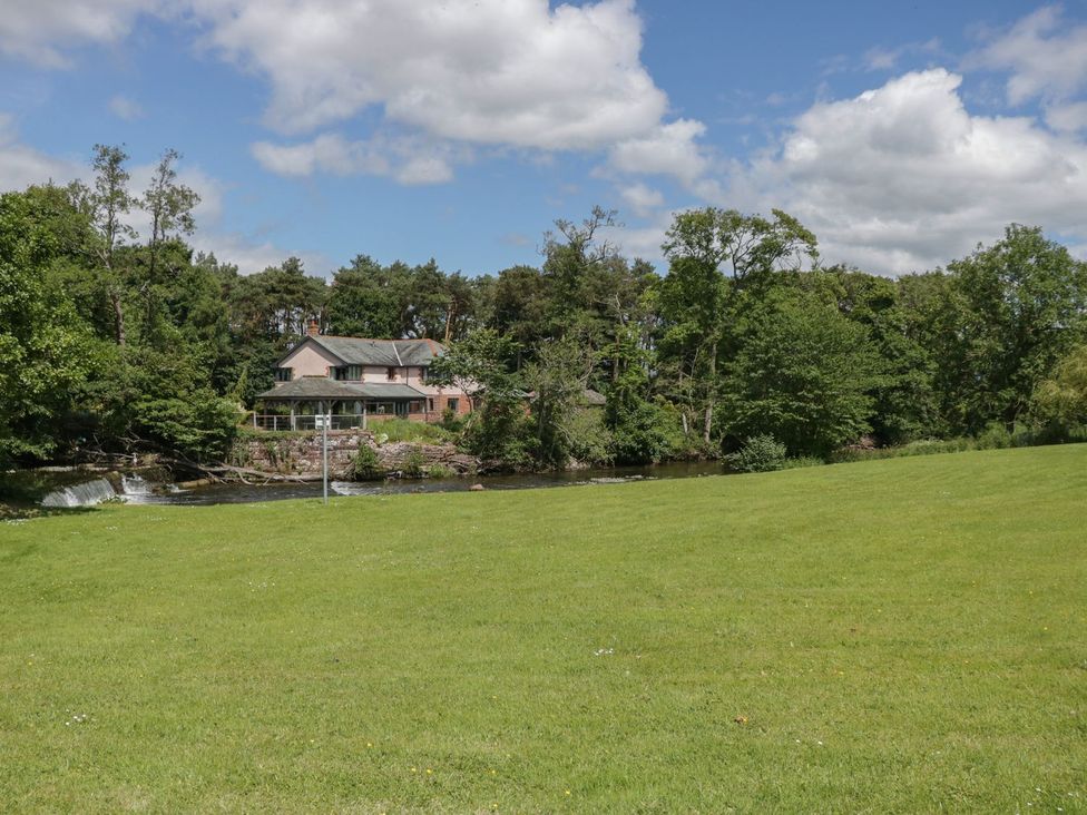 An outdoor view of a house by a river with trees and grass at Bedroom 2 in Penrith