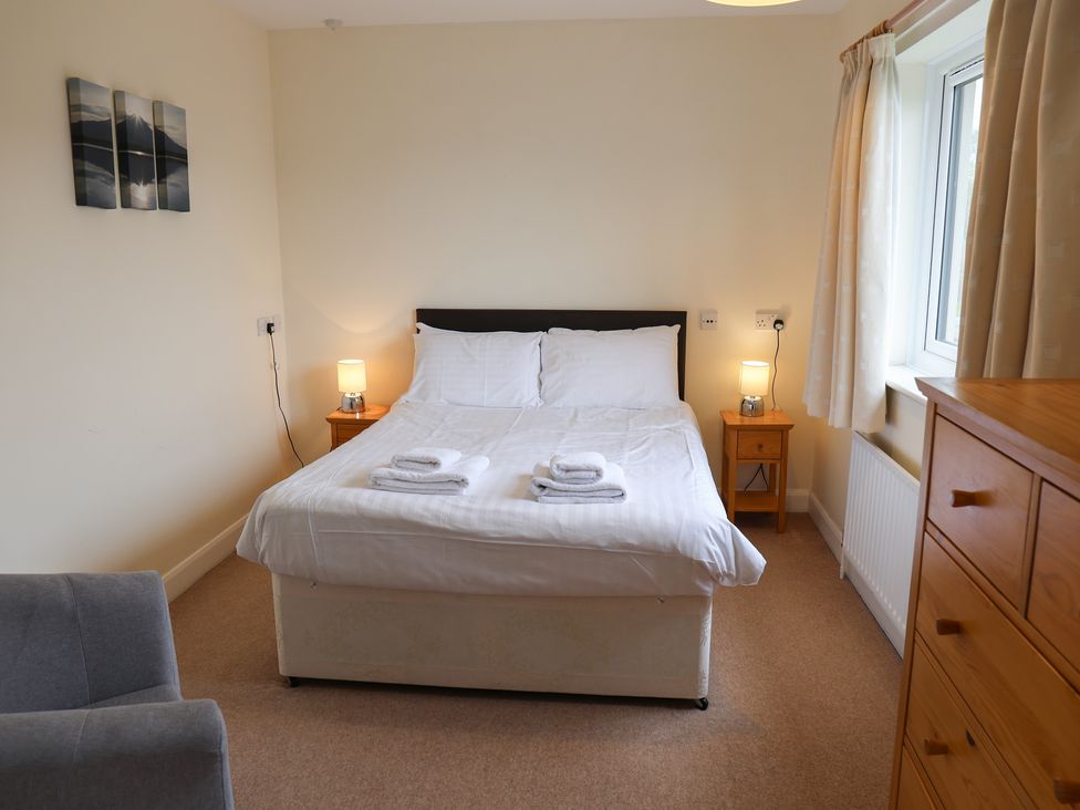 A bedroom with a bed, nightstand, and chair at House 8 Eamont Park in Penrith