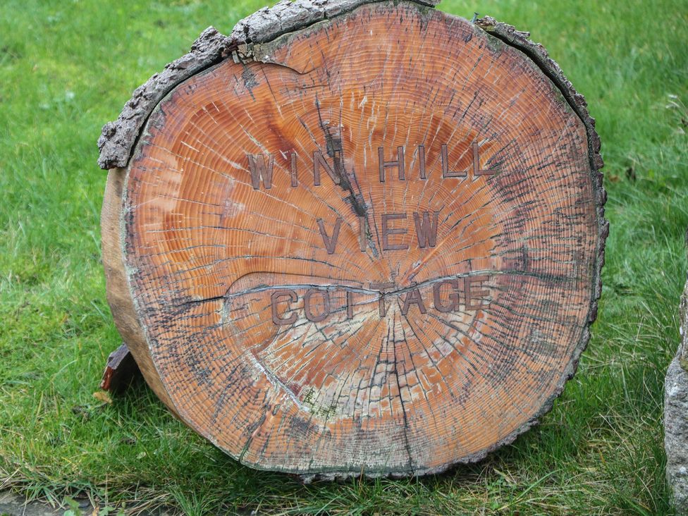 A wooden sign on a tree stump for Win Hill View Cottage in Hope Valley