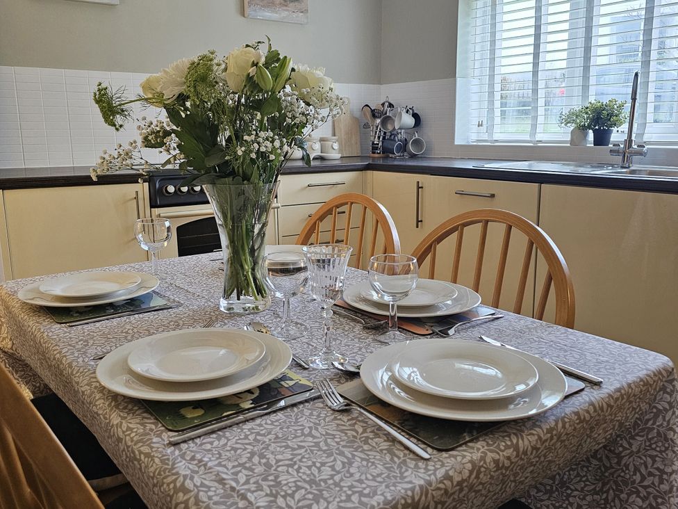 A dining table set with plates and a flower vase at The Cottage On The Green Borth-Y-Gest