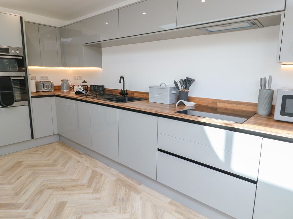 A kitchen with gray units and wooden countertop at Hen Siop Niwbwrch (Newborough)