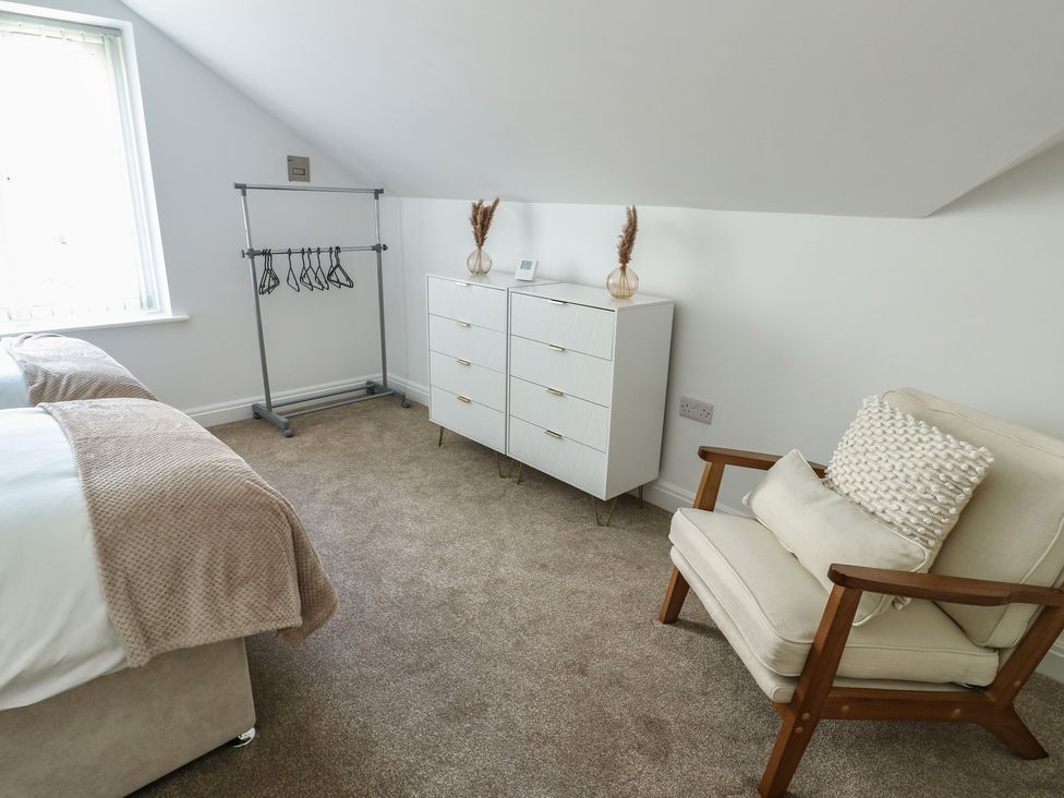 A bedroom with a bed, clothes rack, drawer unit, and chair at Hen Siop, Niwbwrch (Newborough)