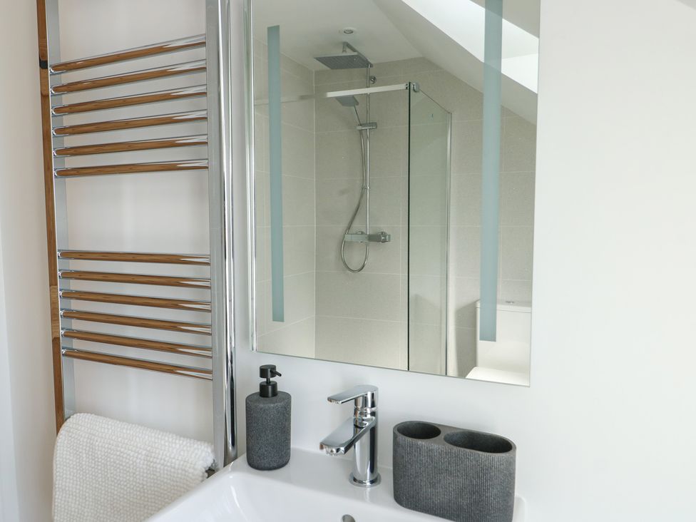 A bathroom with a shower, sink, and towel rail at Hen Siop, Niwbwrch (Newborough)