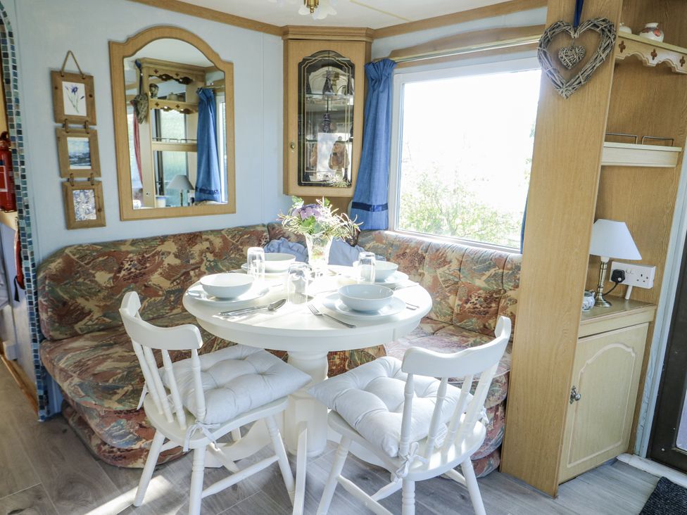 A dining room with a round table and chairs at Meadow Island Caravan Penygroes