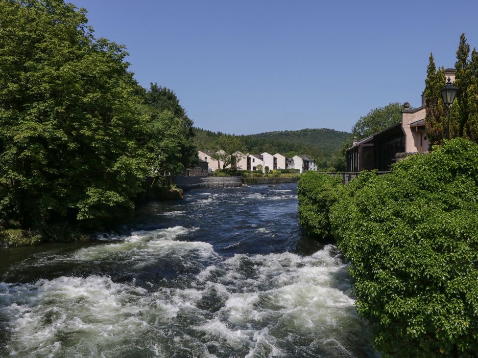 A river flowing with trees and houses in the background at Old Post Office Cottage in Ulverston