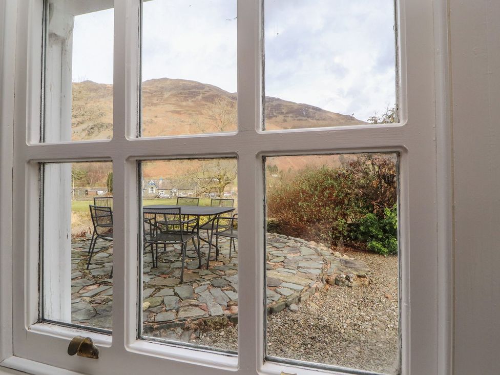 A view of a garden with a table and chairs through a window at Deer How Farm near Glenridding