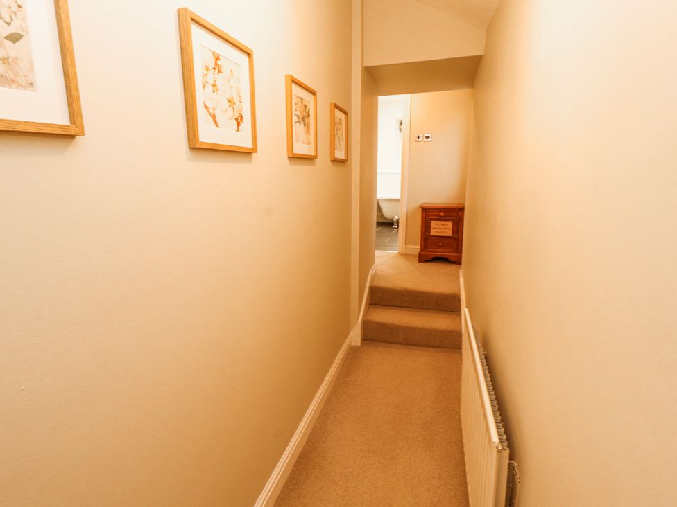A hallway with artwork on walls and a staircase at Deer How Farm in Patterdale near Glenridding
