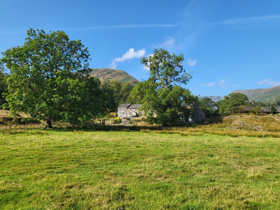 A house and trees in a field near mountains at Deer How Farm in Patterdale near Glenridding