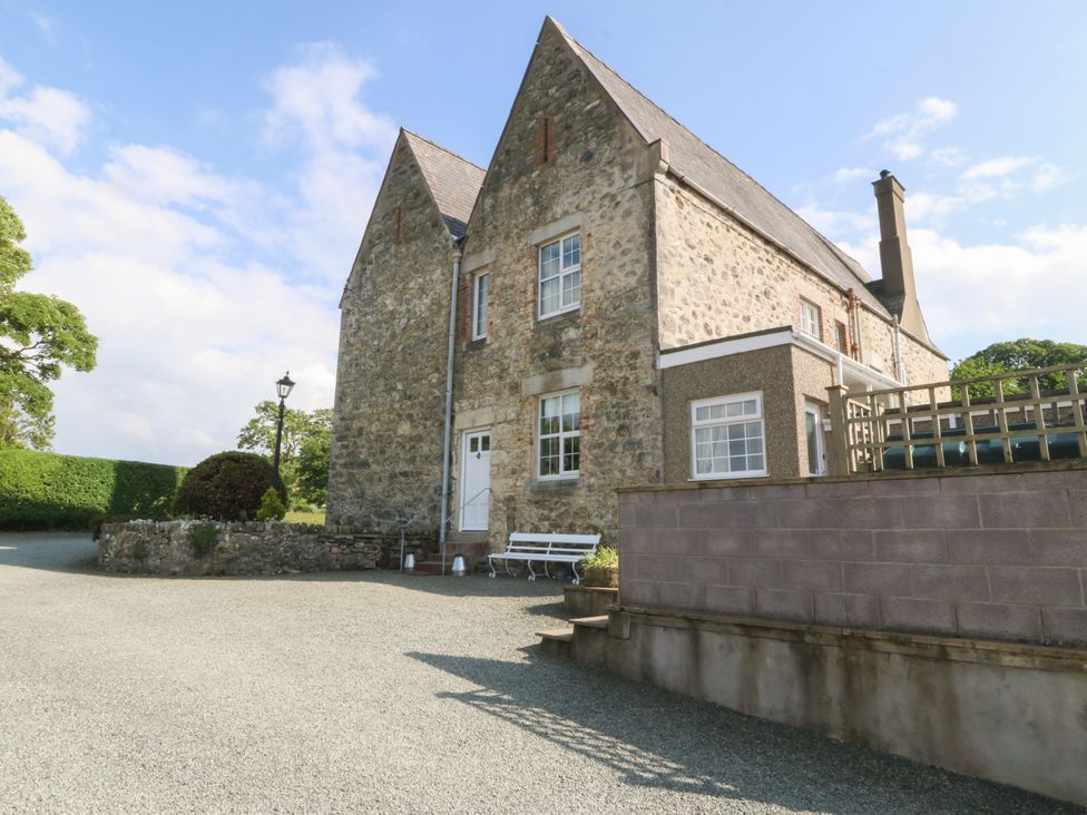 A stone house with multiple windows and a white door next to gravel driveway at Glasfryn in Llandwrog