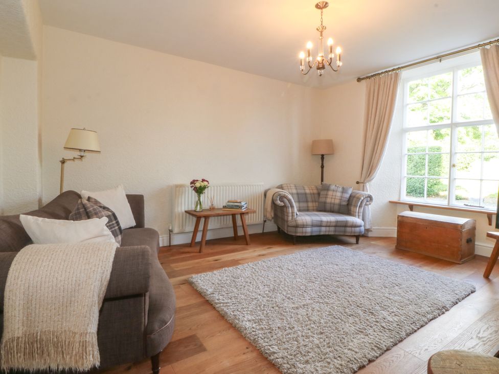 A living room with a brown sofa a plaid armchair a wooden chest and a large window at Glasfryn in Llandwrog