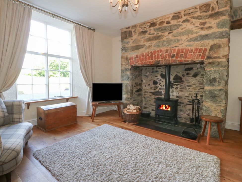 A living room with a stone fireplace a wood stove a television and a chest at Glasfryn in Llandwrog