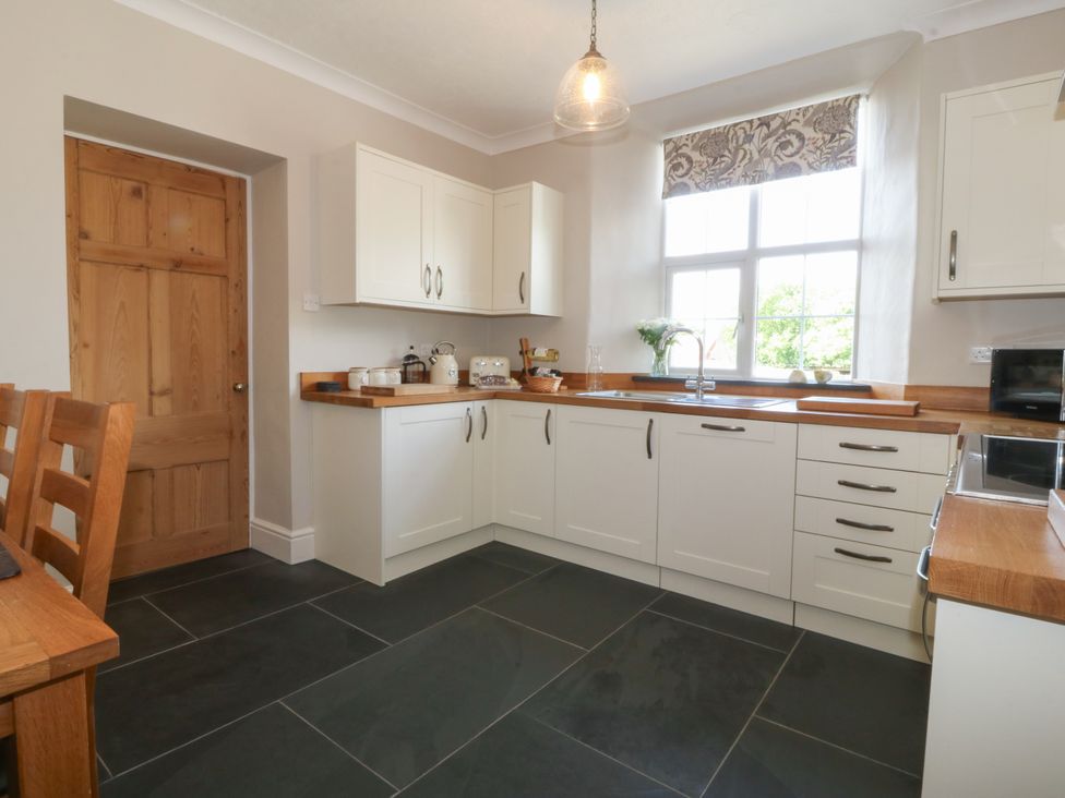 A kitchen with white cabinets wooden countertops a wooden door and large window at Glasfryn in Llandwrog