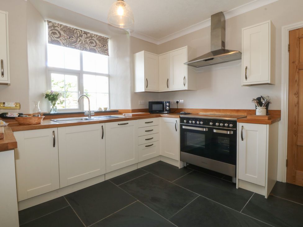A kitchen with white cabinets black tiled floor and a window above the sink at Glasfryn in Llandwrog