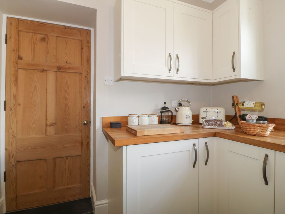 A kitchen corner with white cabinets wooden countertop kitchen appliances and a wooden door at Glasfryn in Llandwrog