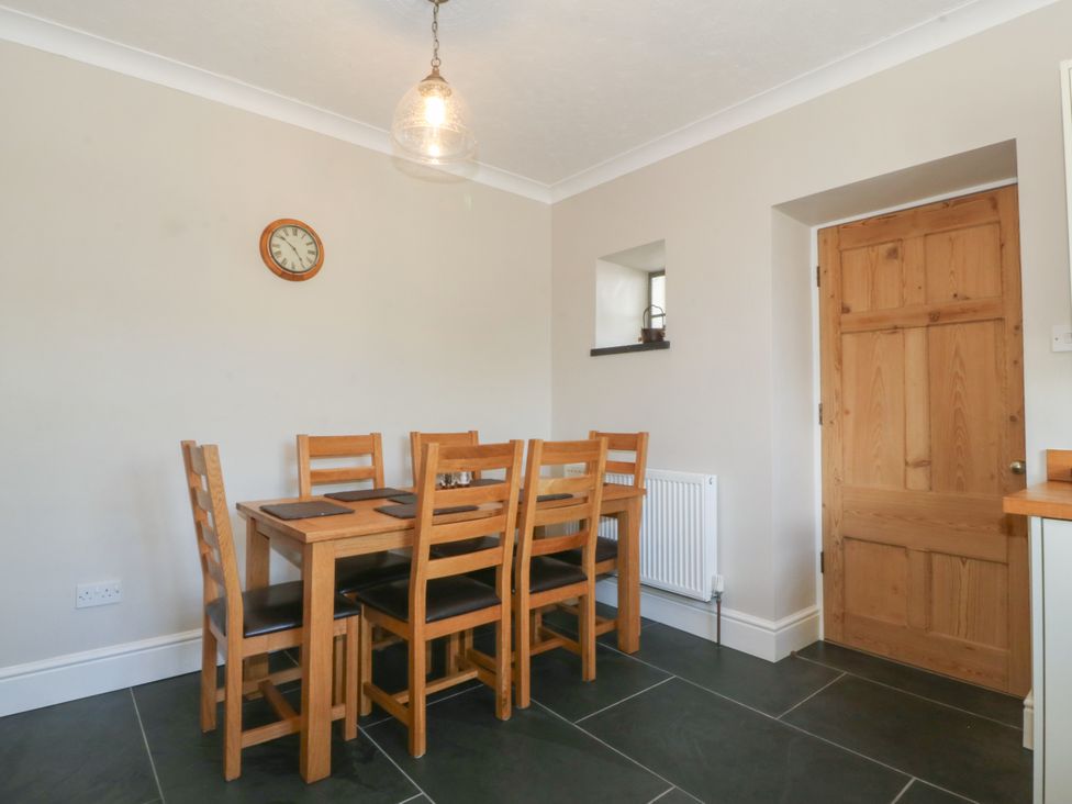 A dining area with a wooden table and six chairs a wall clock a wooden door and a small window at Glasfryn in Llandwrog